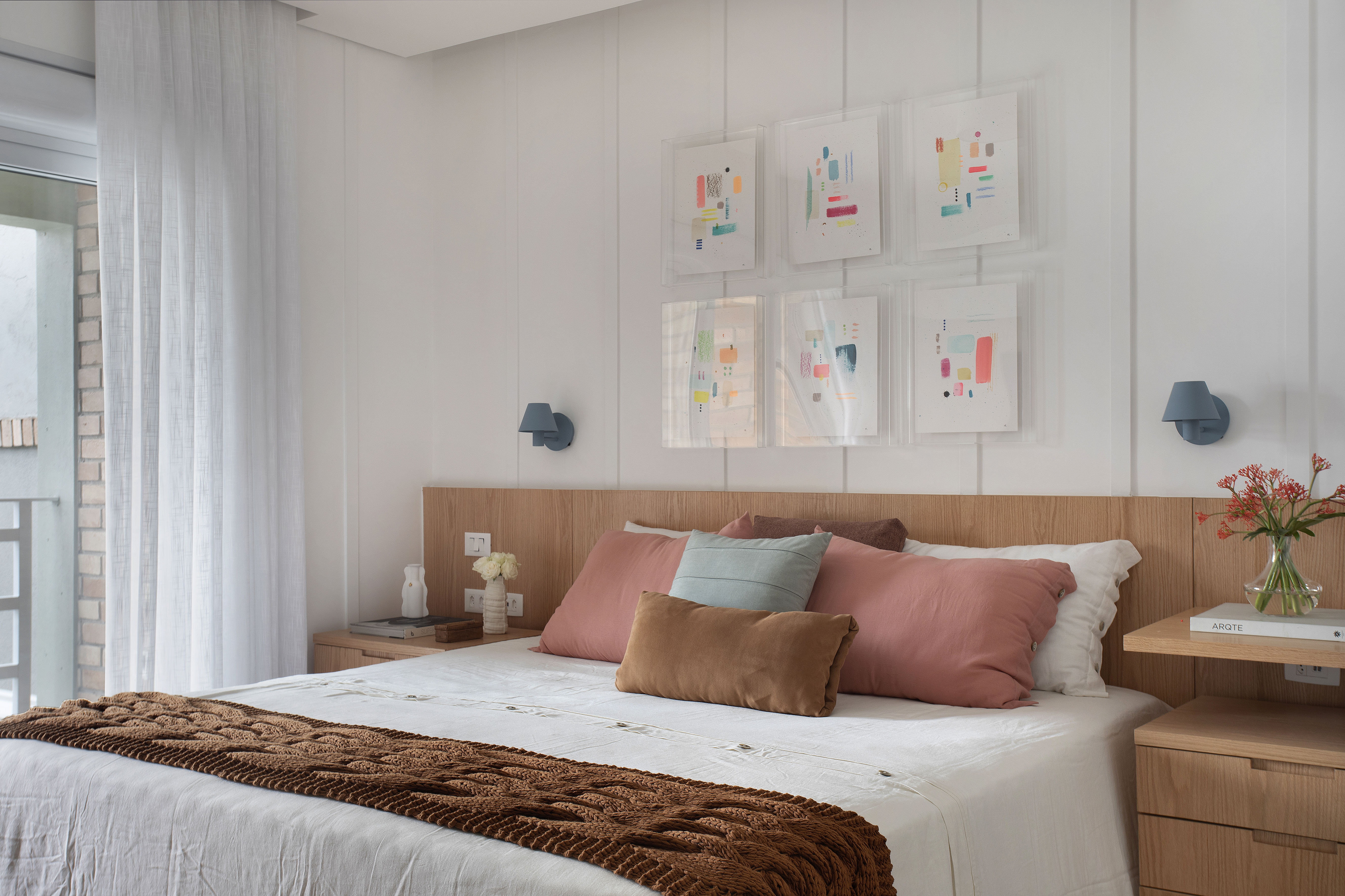 Quarto com cama de casal e cabeceira de madeira e quadros em cima da cama.