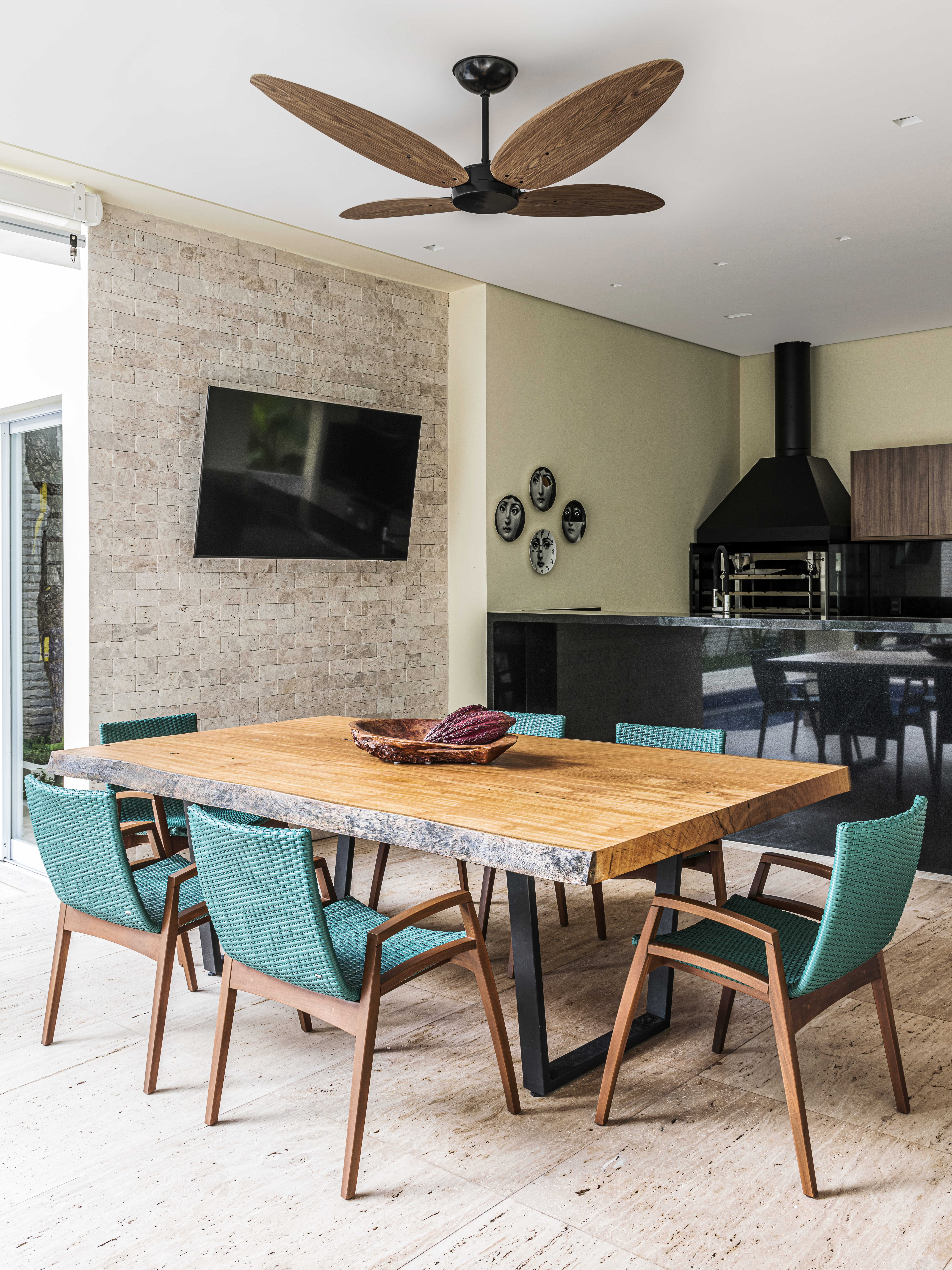 Área gourmet com churrasqueira, mesa com tampo de madeira e cadeiras azul esverdeadas.