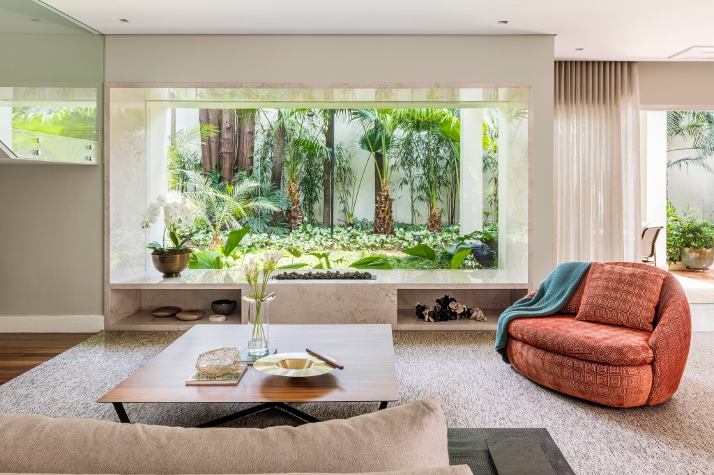 Sala de estar integrada com jardim; sofá branco, tapete claro, estante embaixo de escada, poltrona vermelha.