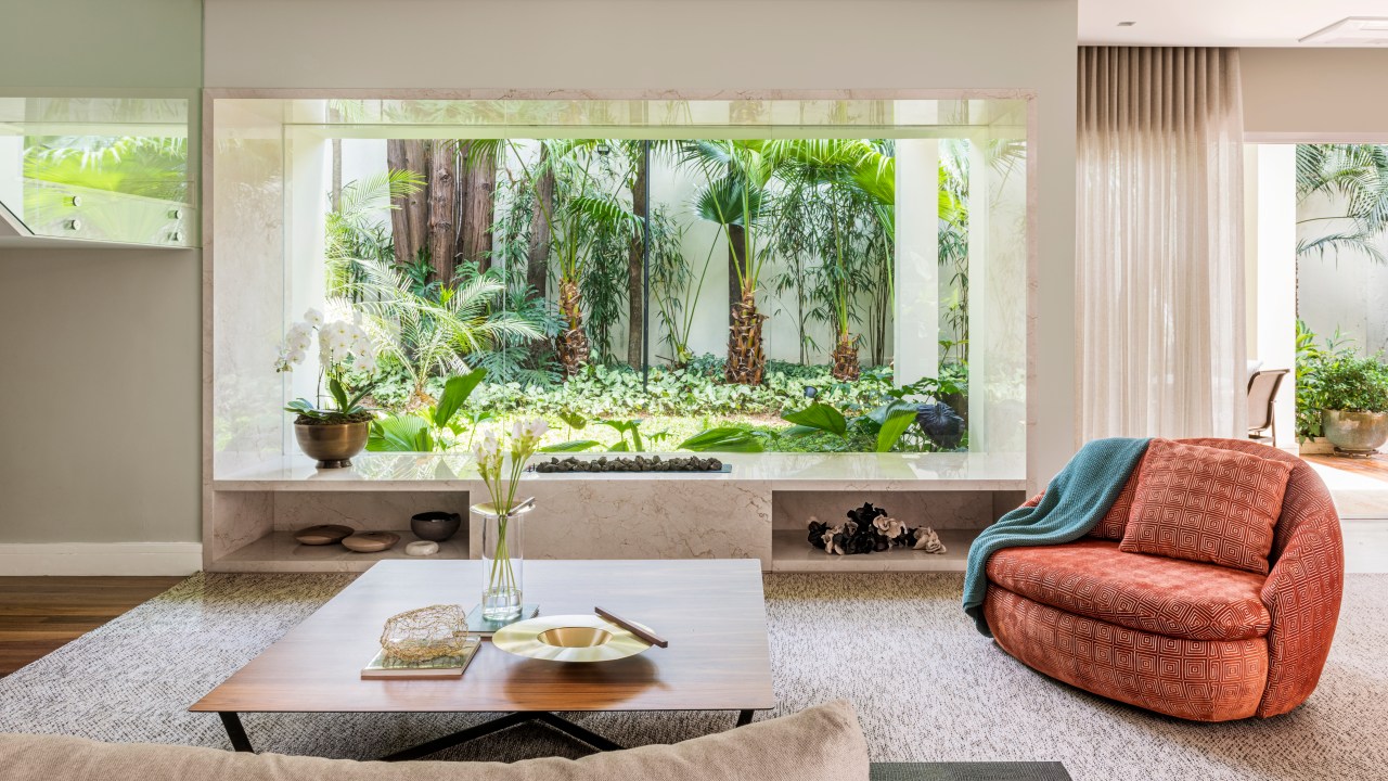 Sala de estar integrada com jardim; sofá branco, tapete claro, estante embaixo de escada, poltrona vermelha.