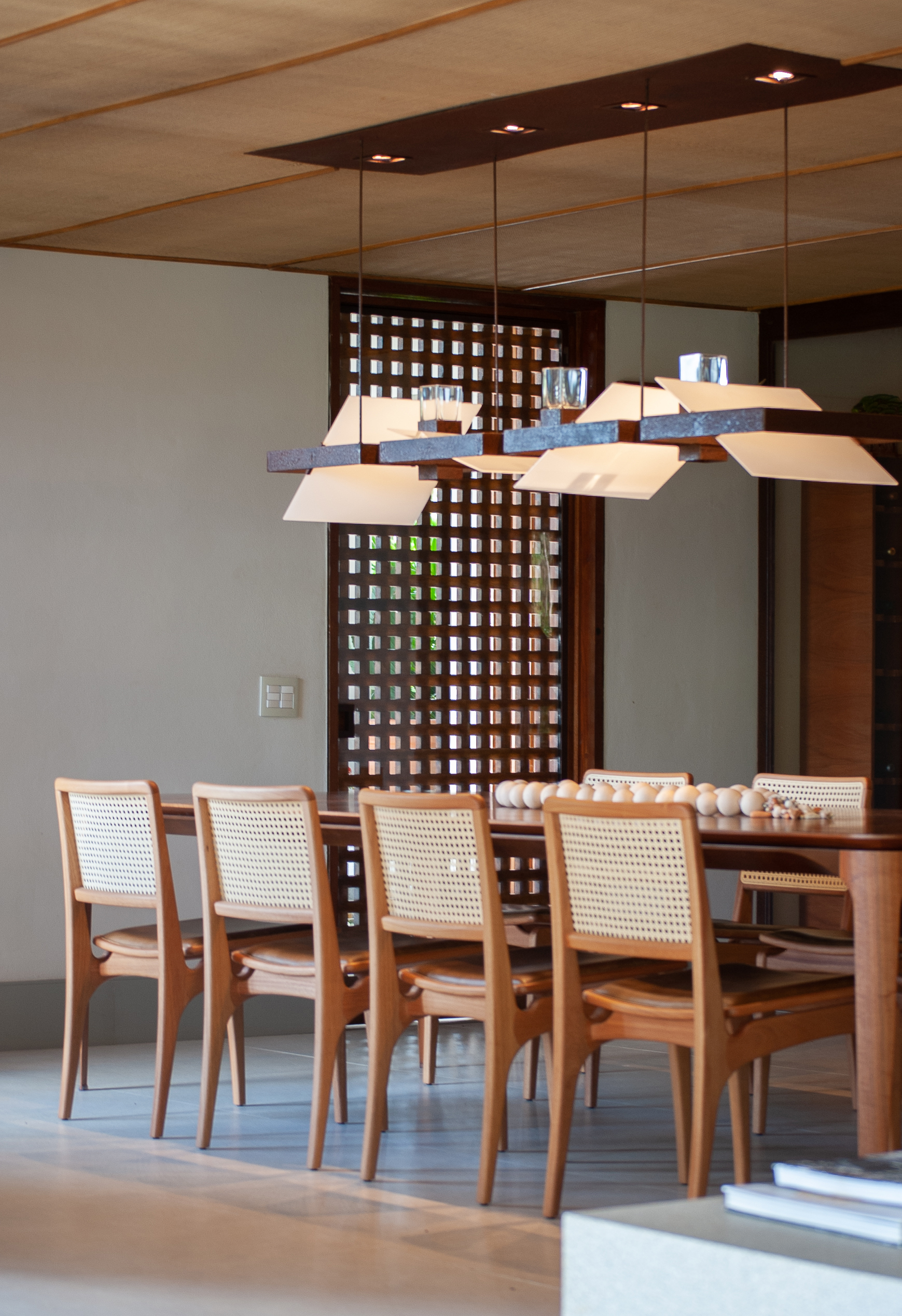 Sala de jantar com mesa de madeira e cadeiras de madeira com encosto de palha, luminária.