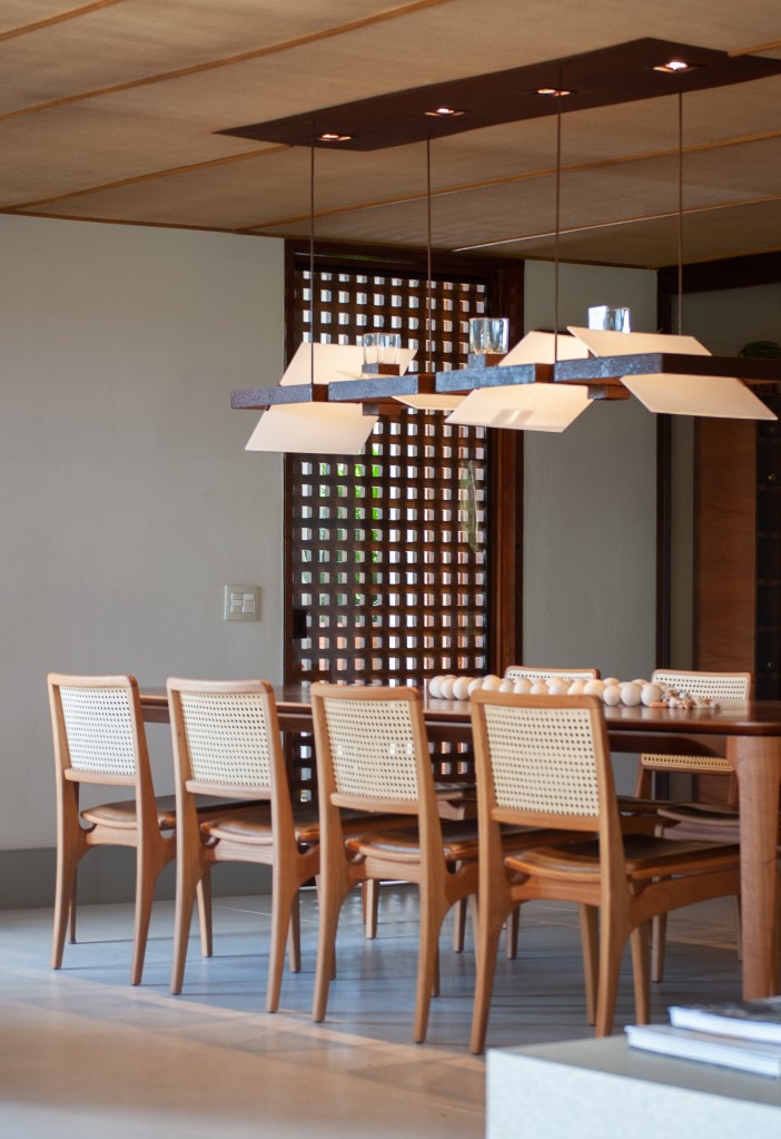 Sala de jantar com mesa de madeira e cadeiras de madeira com encosto de palha, luminária.