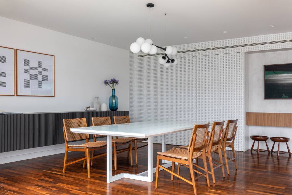 Sala de jantar com mesa de seis lugares branca e cadeiras de madeira.