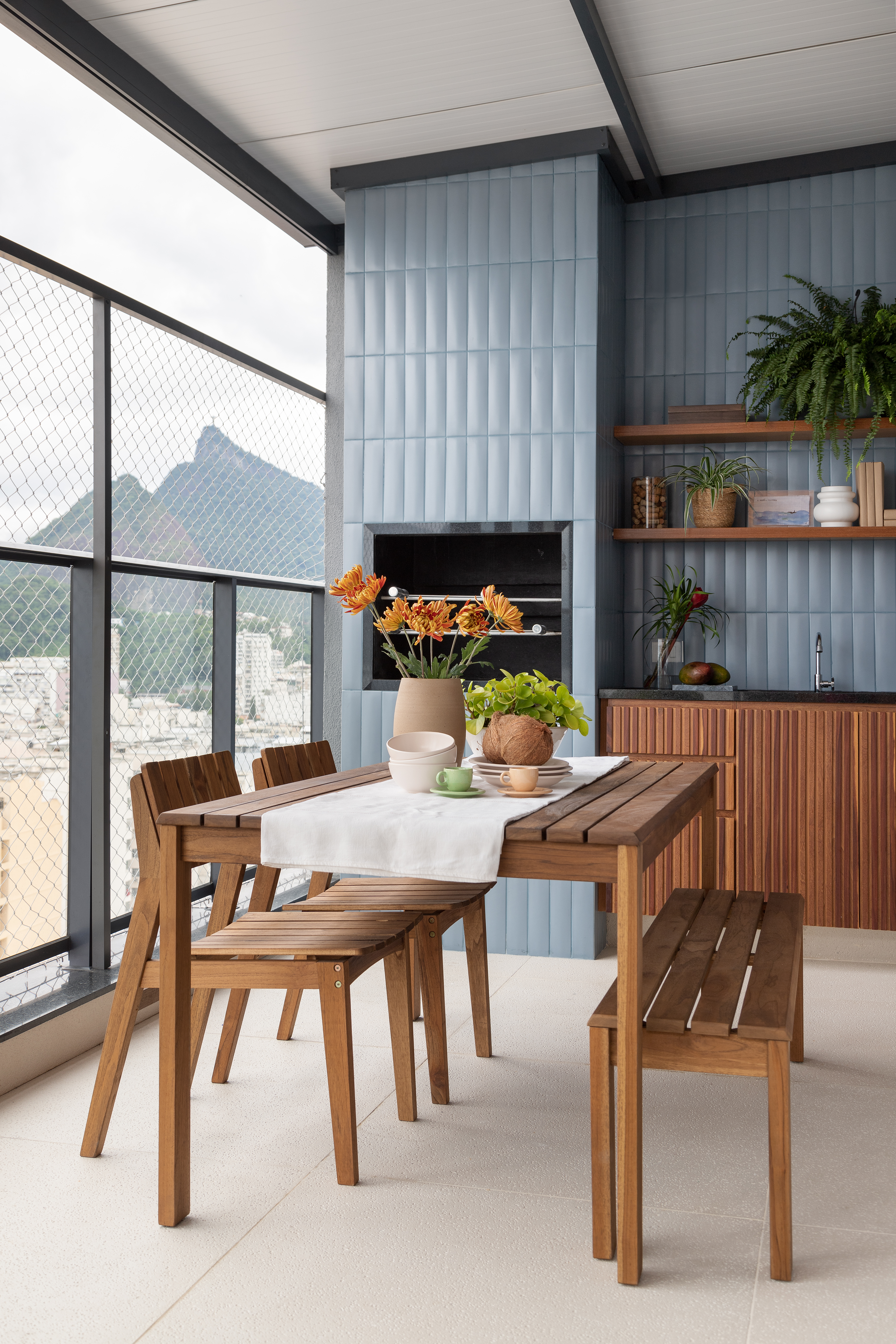 Área gourmet; varanda gourmet com churrasqueira, mesa de madeira e parede revestida de azulejos azuis.