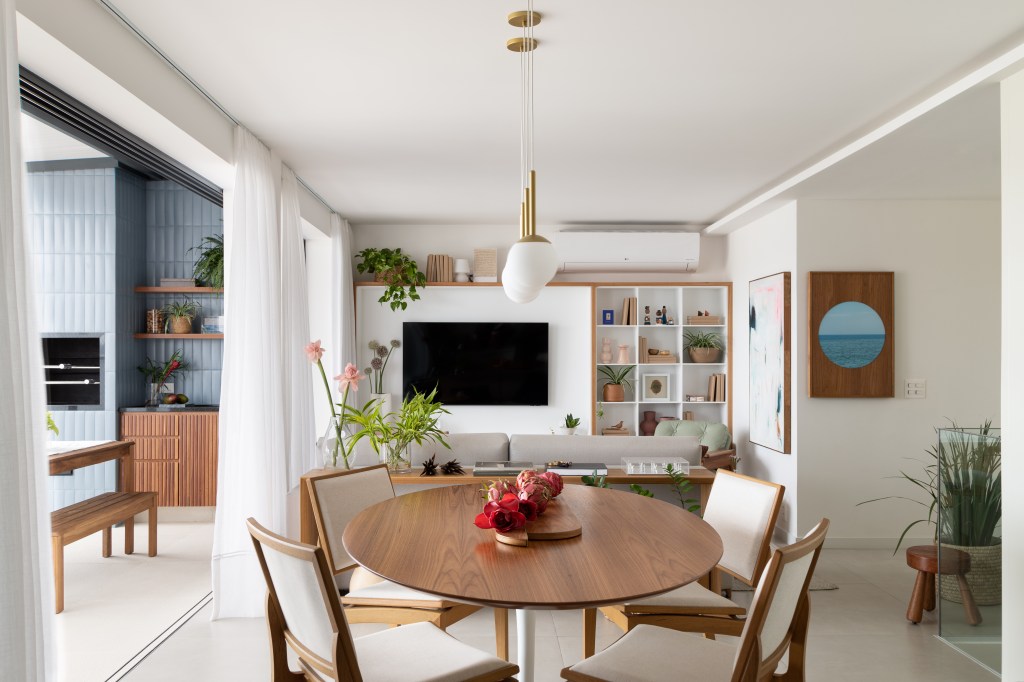 Sala de estar integrada com jantar; estante de nichos branca, mesa redonda de madeira.