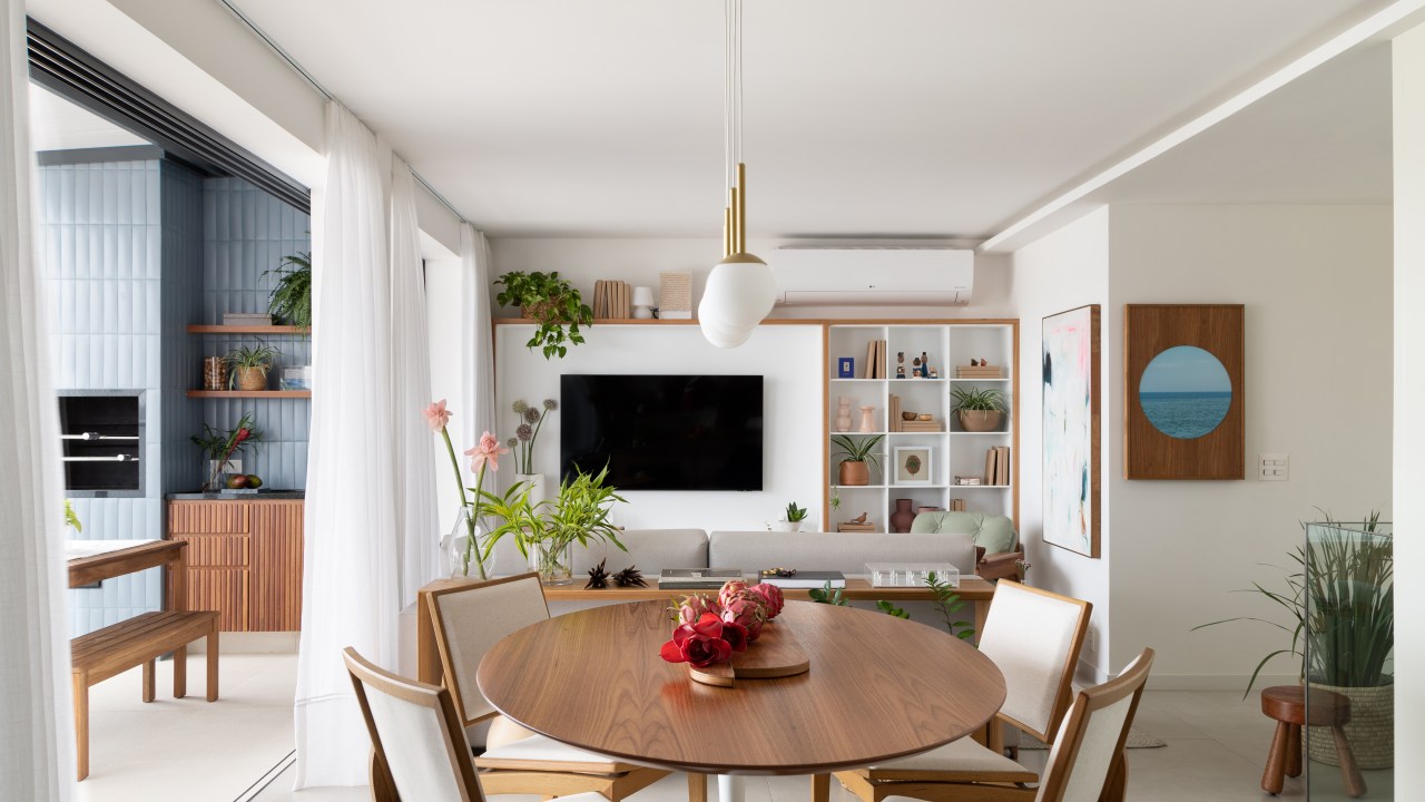 Sala de estar integrada com jantar; estante de nichos branca, mesa redonda de madeira.