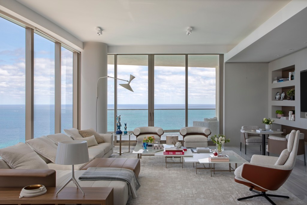 Sala de estar branca com vista para o mar, sofá e poltrona branca, luminária branca de piso e mesa de centro.