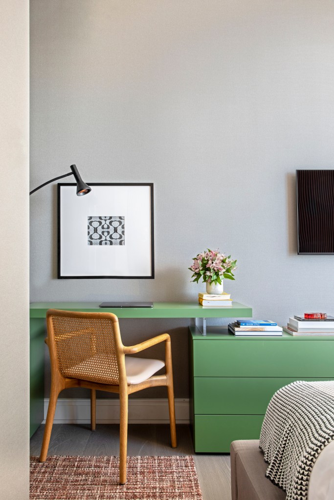 Home office com mesa e gaveteiro verde, cadeira de madeira e luminária lateral.