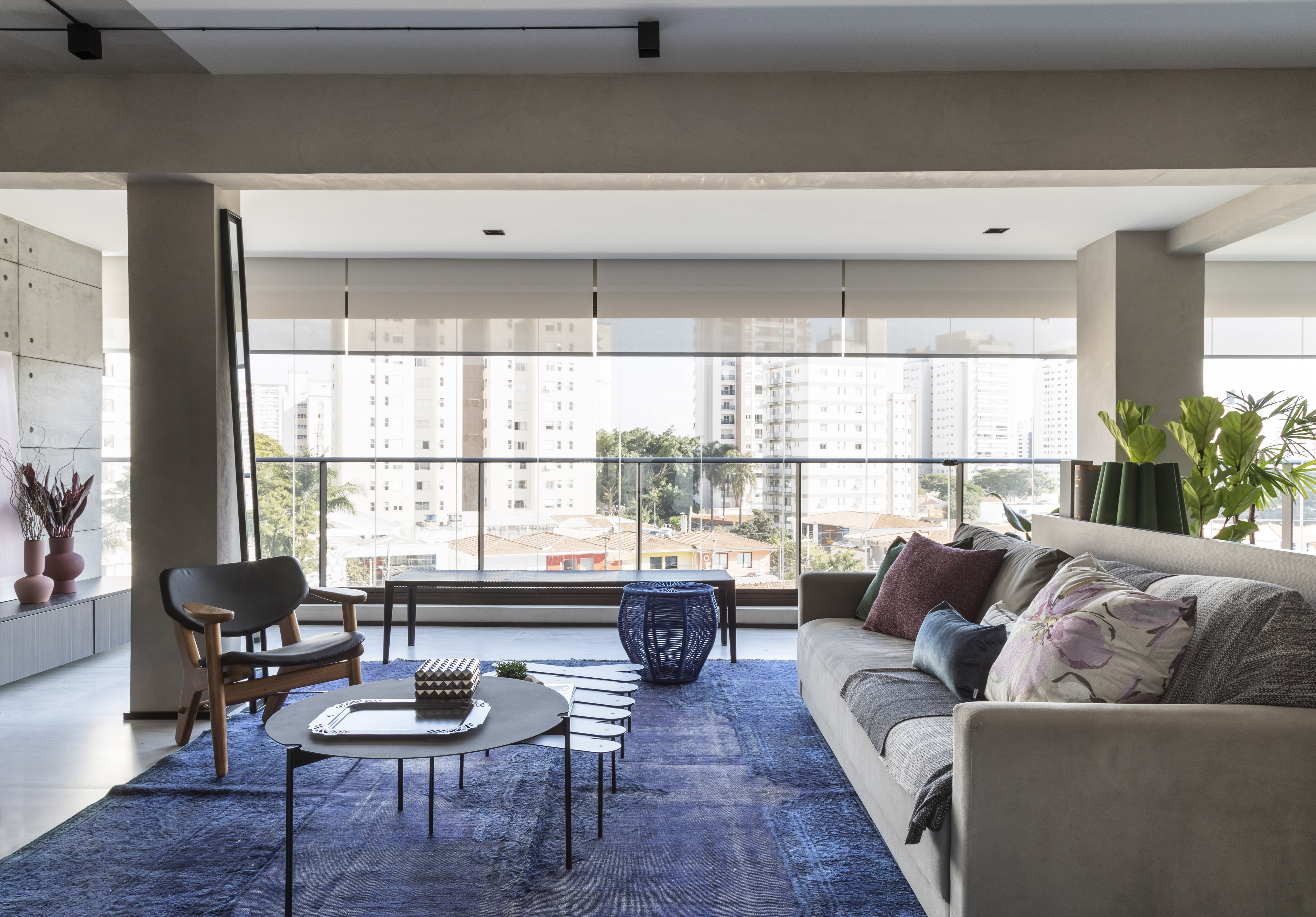 Sala de estar integrada com varanda com poltrona, sofá cinza e tapete azul.