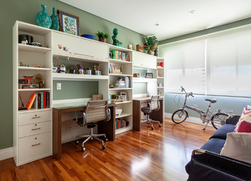 Home office para duas pessoas com marcenaria branca, piso de madeira e parede verde.