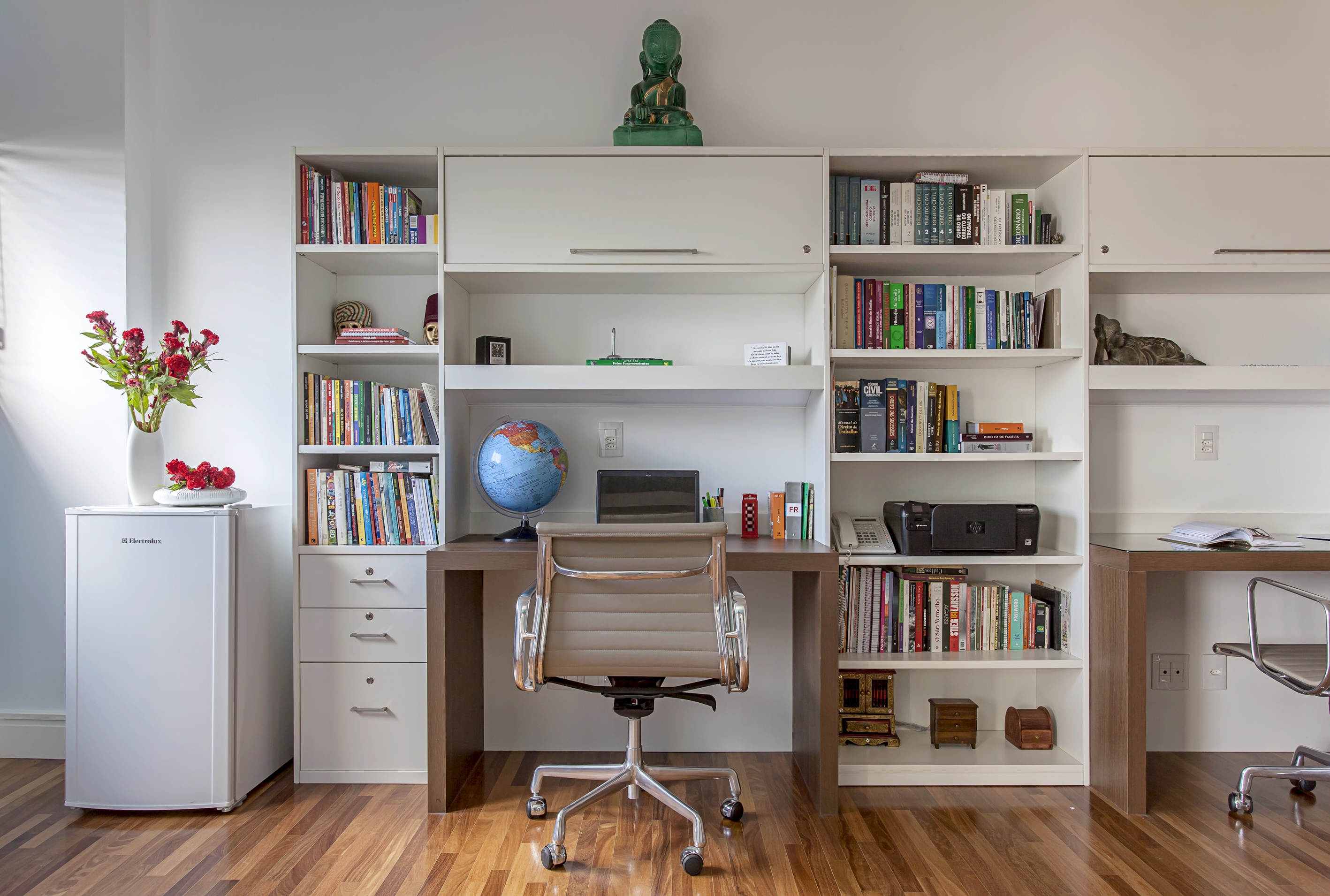 Home office com marcenaria branca, bancada de trabalho e estante de livros.