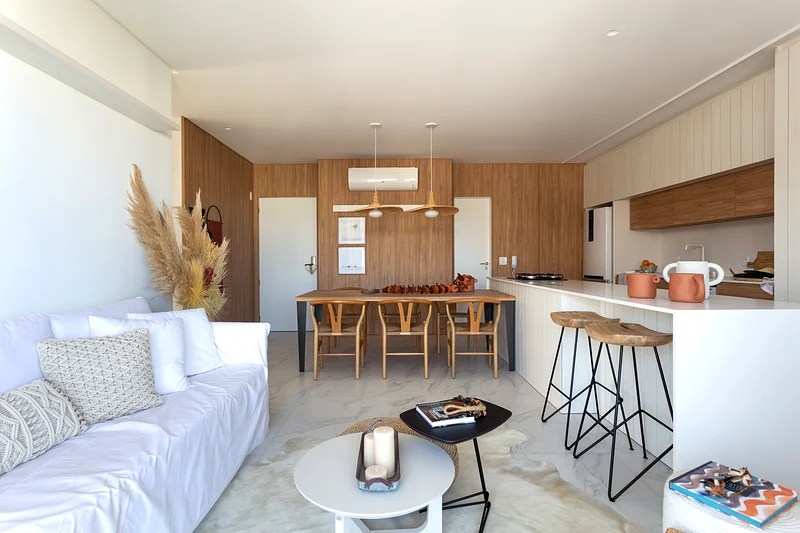 Sala de estar integrada com parede revestida de madeira, sofá branco e mesa de centro.