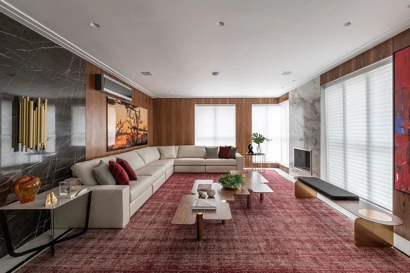 Sala de estar com sofá claro, parede revestida de madeira e tapete avermelhado.
