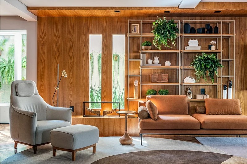Sala de estar com paredes revestidas de madeira, poltrona com pufe e sofá.