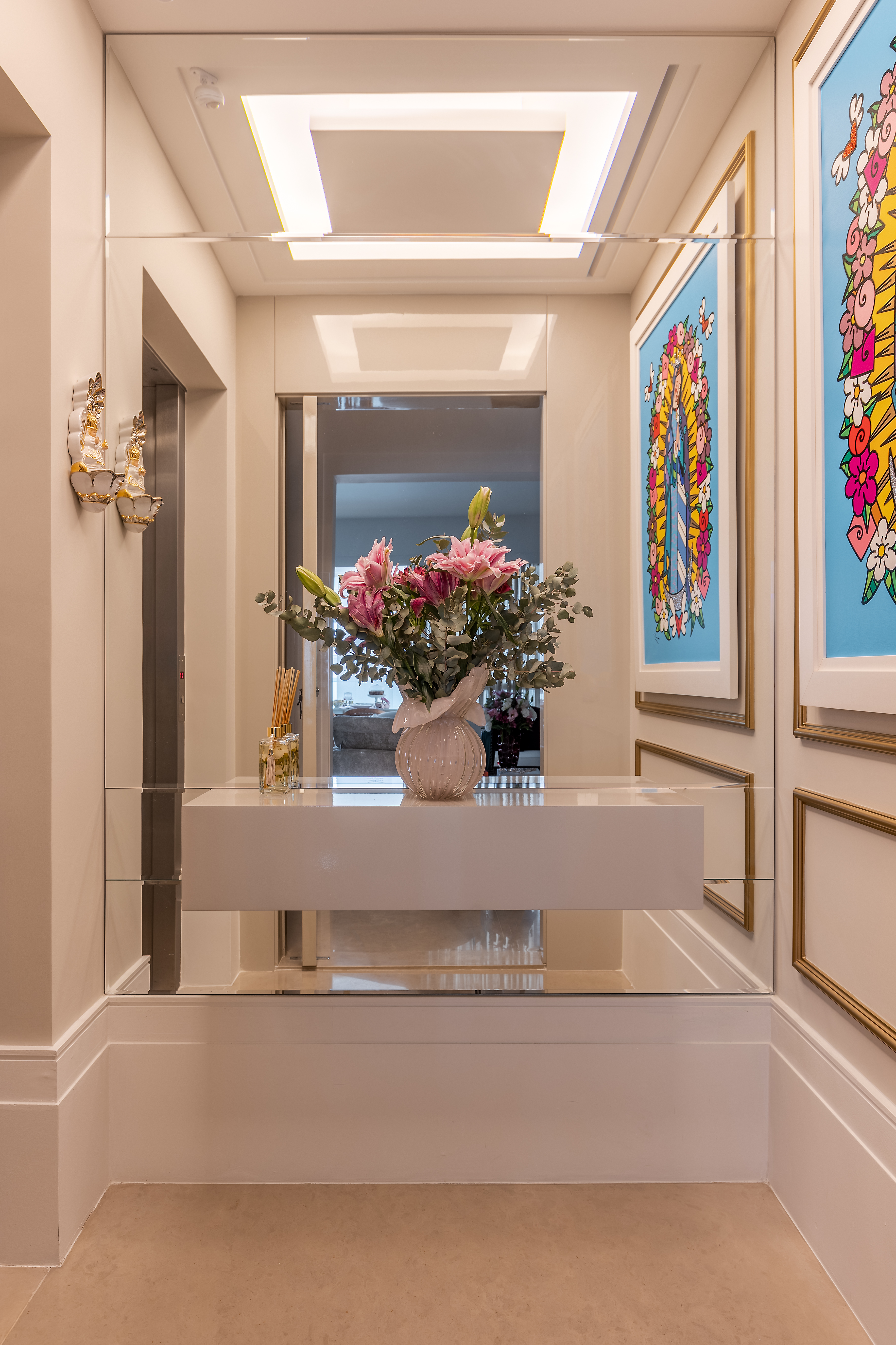 Hall de entrada com espelho, aparador, vaso de flores e quadro.