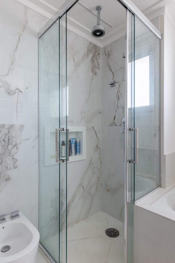 Banheiro com box de vidro e paredes com revestimento marmorizado.