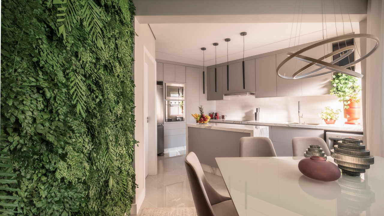 Sala de jantar integrada com cozinha e jardim vertical com plantas preservadas.