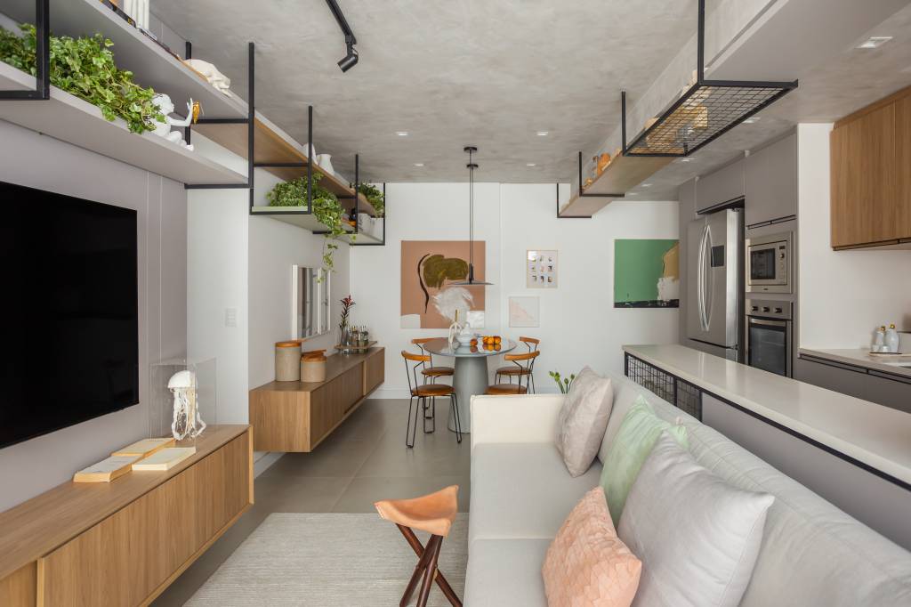 Sala de estar integrada com piso de porcelanato, sofá branco, rack de madeira e sala de jantar com mesa redonda.