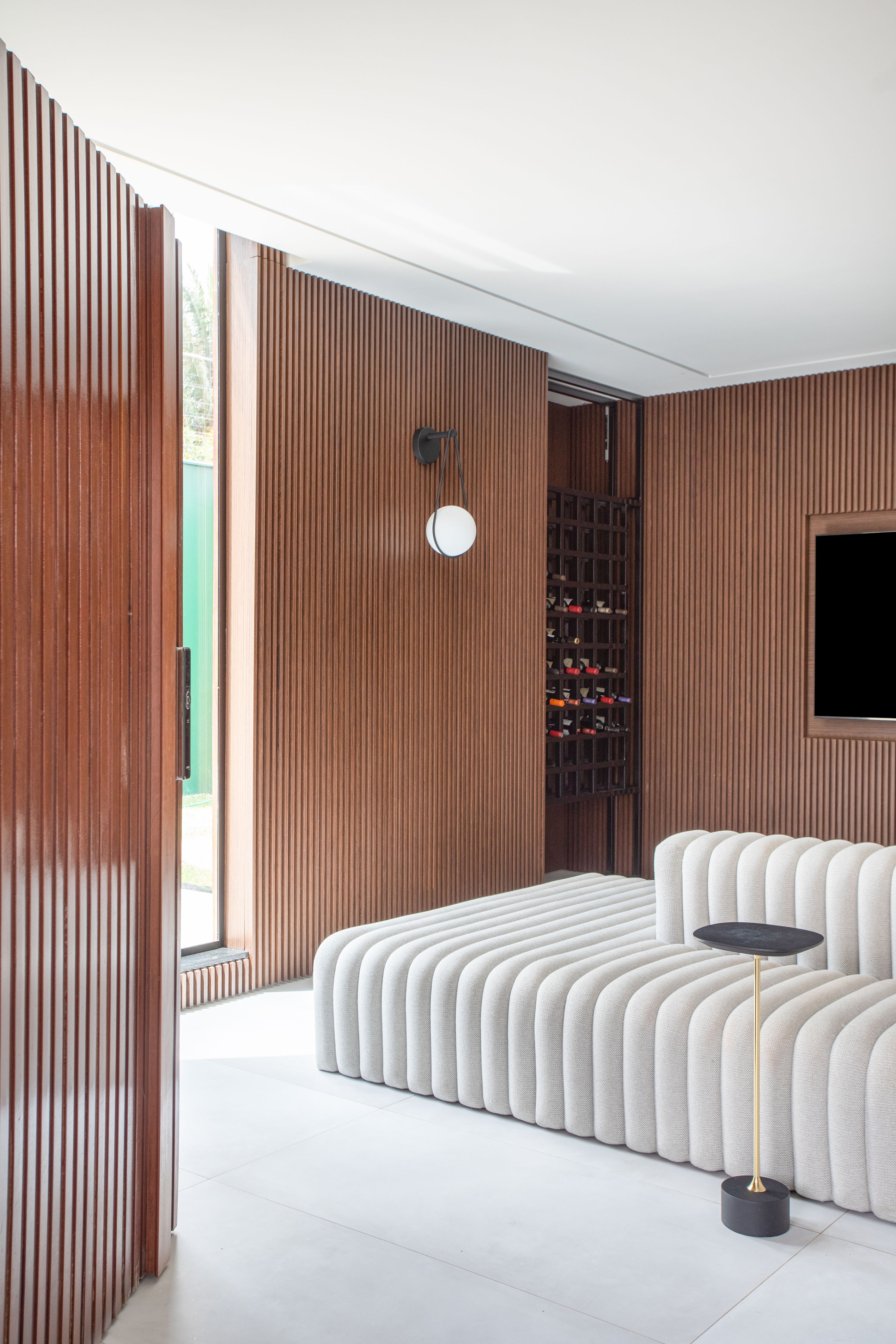 Sala com sofá ilha branco e parede revestida de madeira.