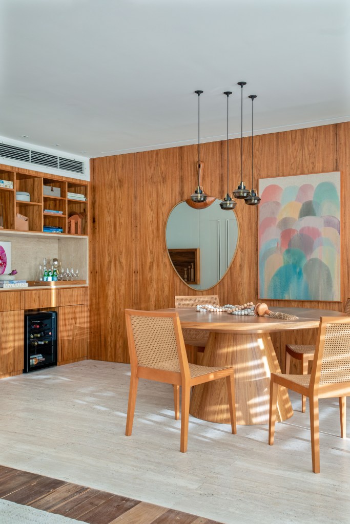 Sala de jantar com paredes revestidas de madeira, mesa redonda de madeira, cadeira com encosto de palhinha e espelho.