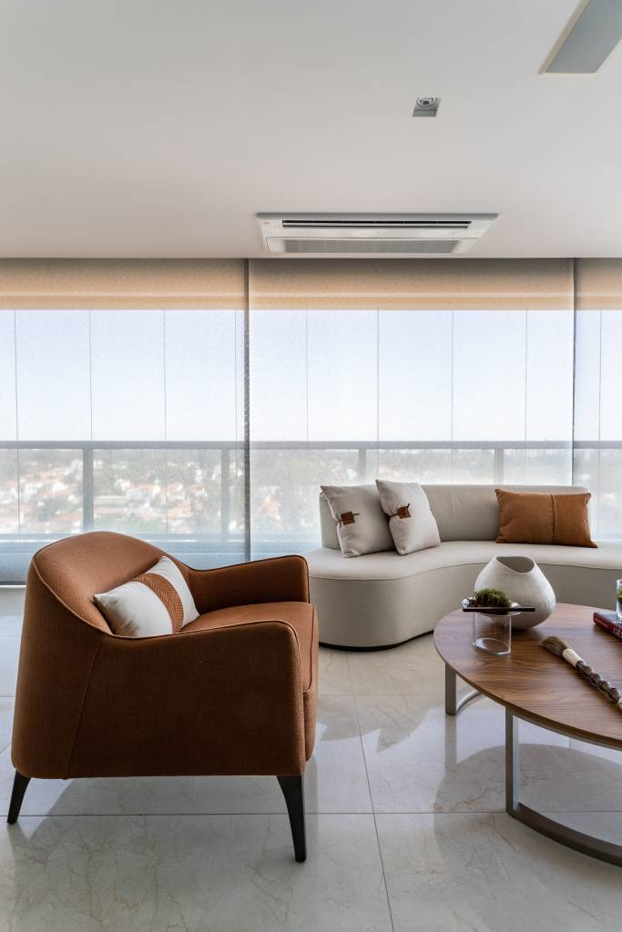 Varanda integrada com piso de porcelanato, poltrona em tom terroso e sofá curvo branco.