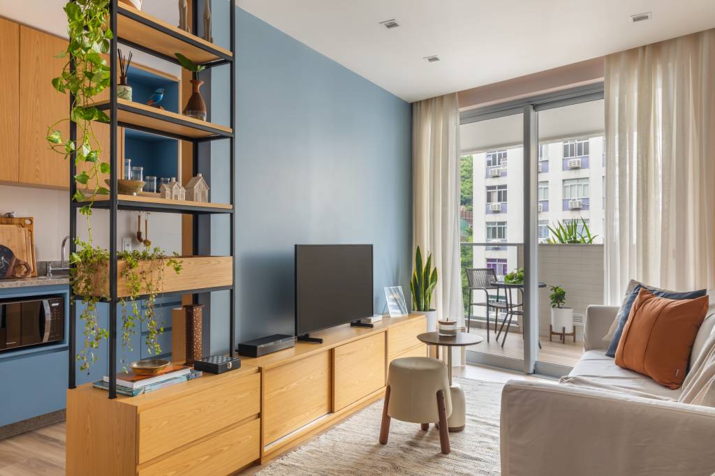 Sala de estar estreita com parede azul, rack de madeira e estante vazada.