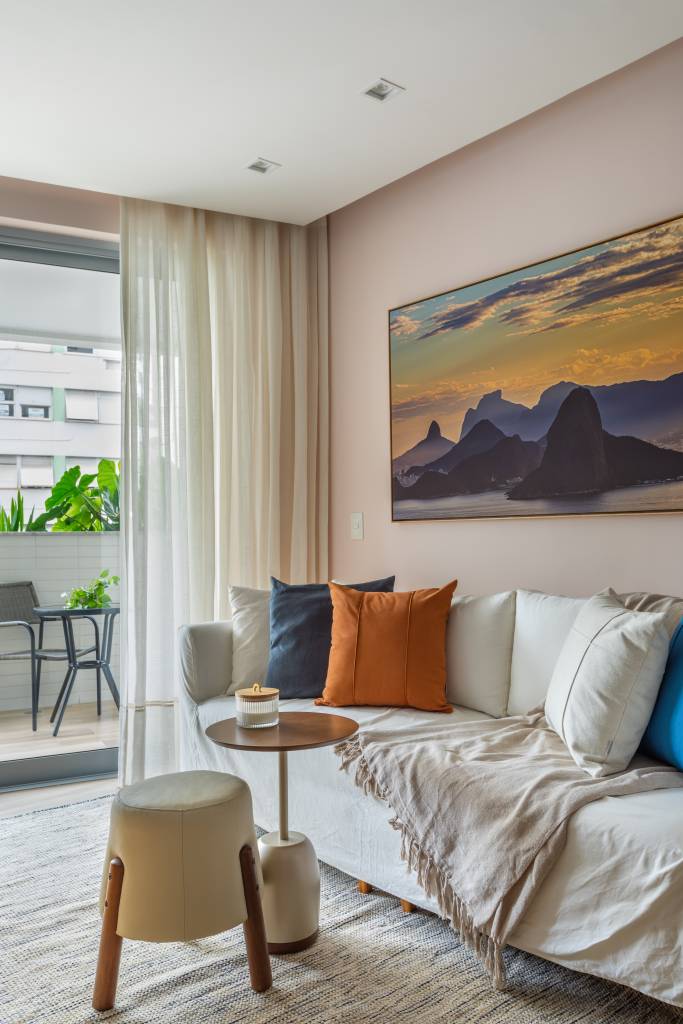Sala de estar com sofá branco, pufe pequeno e almofadas coloridas.