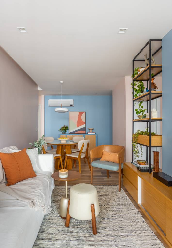 Sala de estar estreita integrada com jantar; sofá claro e estante vazada.