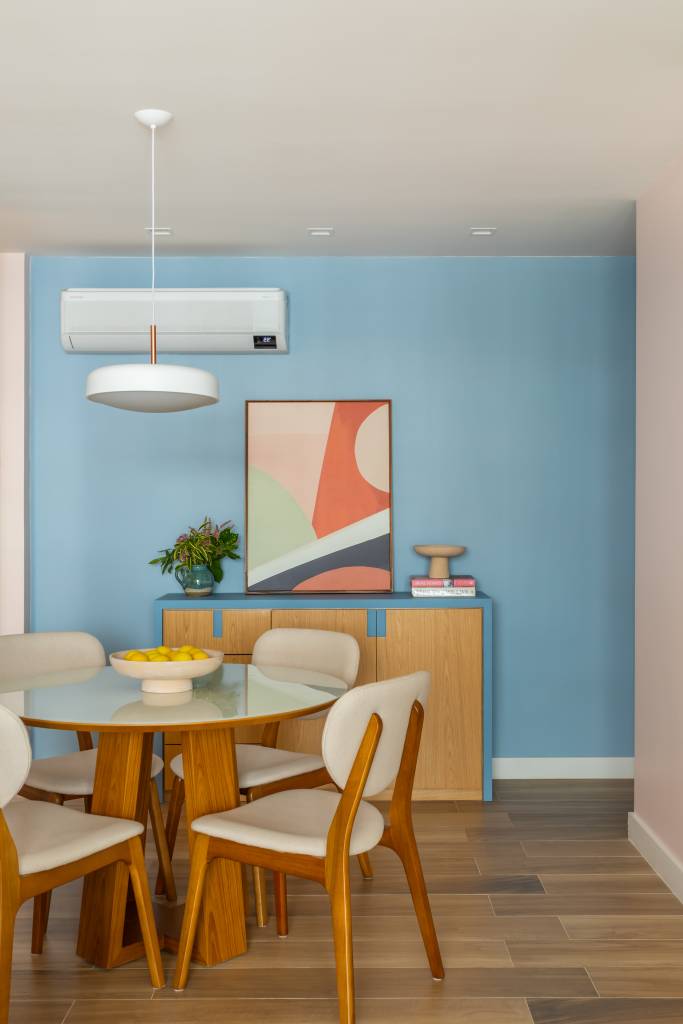 Sala de jantar com parede azul, mesa de jantar redonda, cadeiras com estofamento branco.