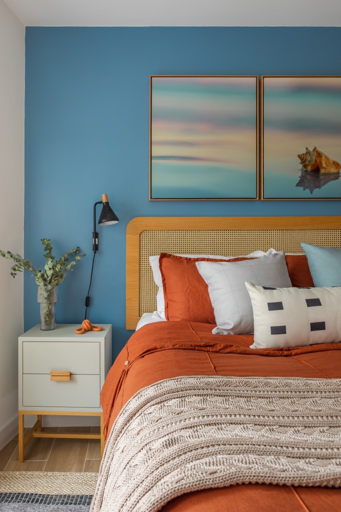Quarto com parede azul, cabeceira de palhinha e armário de madeira.