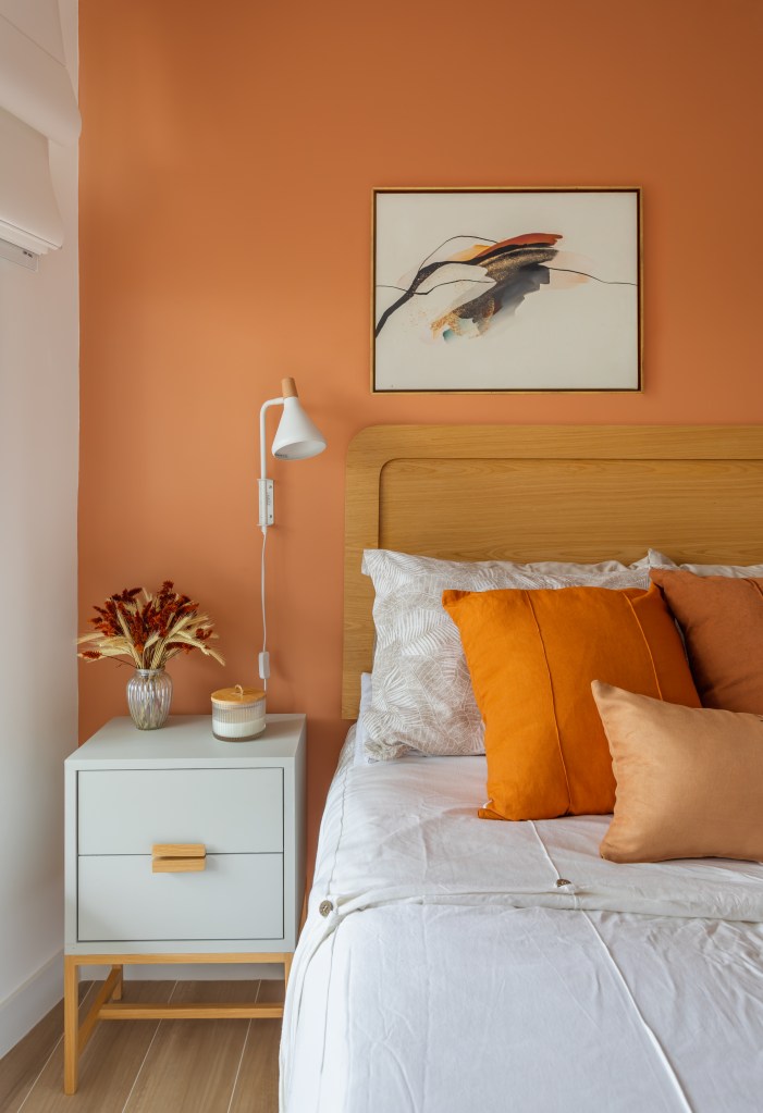 Quarto com parede laranja, cama de casal, armário com porta branca e cabeceira de madeira.