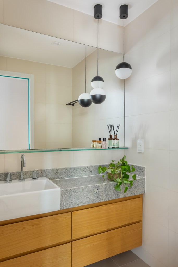 Banheiro claro com bancada de granito, cuba branca e luminárias esféricas.