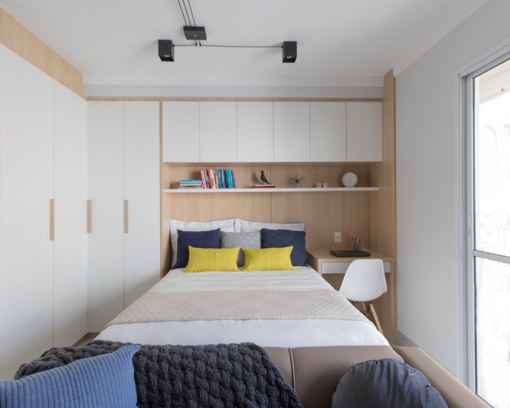 Apartamento pequeno de 29 m² possui lavanderia, home office e cama de casal, Projeto de Letícia de Nóbrega. Na foto, quarto de casal com armários brancos e home office.