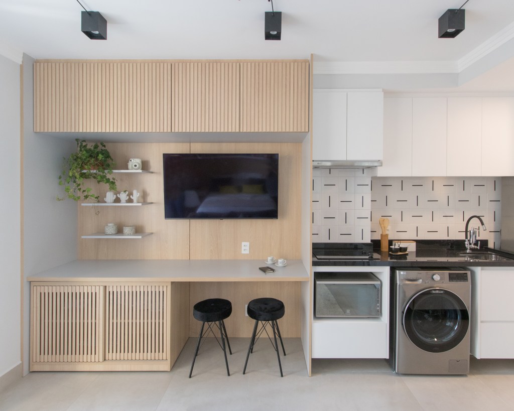 Apartamento pequeno de 29 m² possui lavanderia, home office e cama de casal, Projeto de Letícia de Nóbrega. Na foto, cozinha integrada com sala, espaço de refeições e tv.