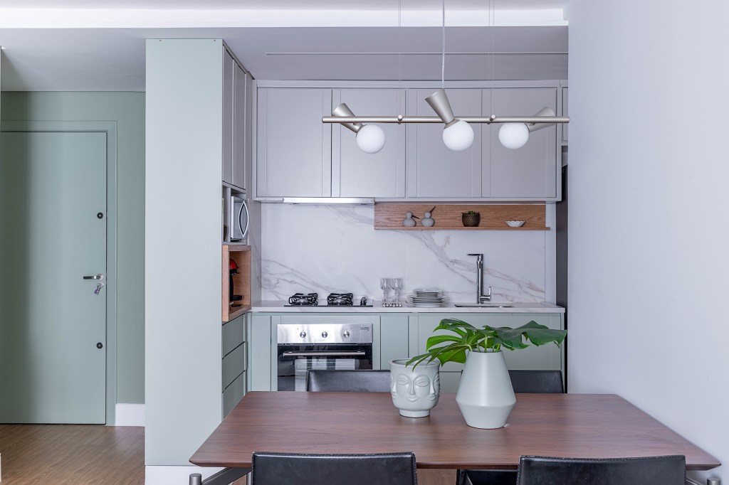 Cozinha pequena integrada com marcenaria verde clara.