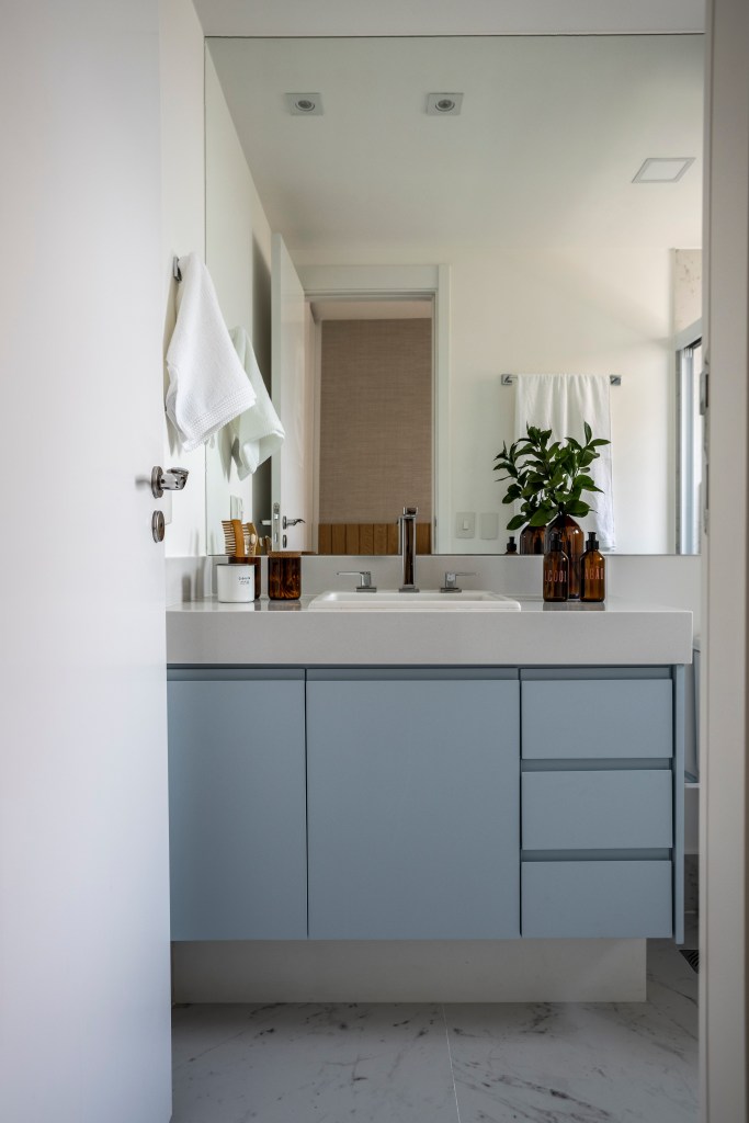 Apê de 110 m² com pé-direito duplo vira duplex com mezanino metálico, Na foto, banheiro com marcenaria azul e espelho. NA foto, banheiro com marcenaria azule espelho.