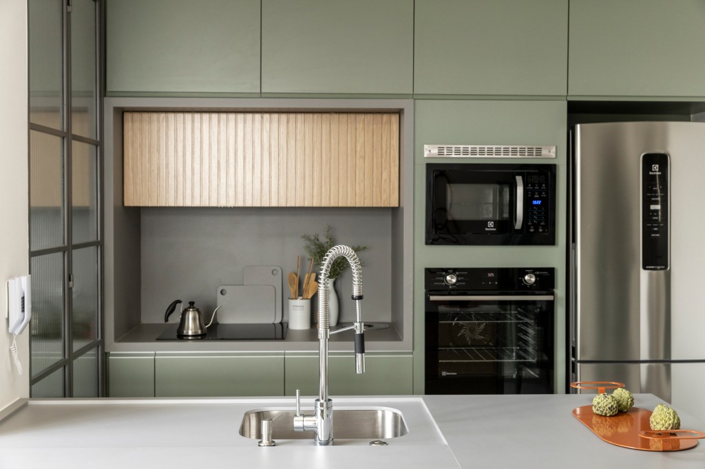 Apê de 110 m² com pé-direito duplo vira duplex com mezanino metálico. Na foto, cozinha integrada com marcenaria verde e torre quente.