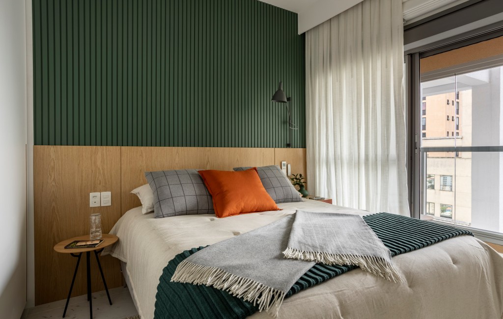 Apê de 110 m² com pé-direito duplo vira duplex com mezanino metálico. Na foto, quarto de casal com parede ripada verde e cabeceira de madeira.