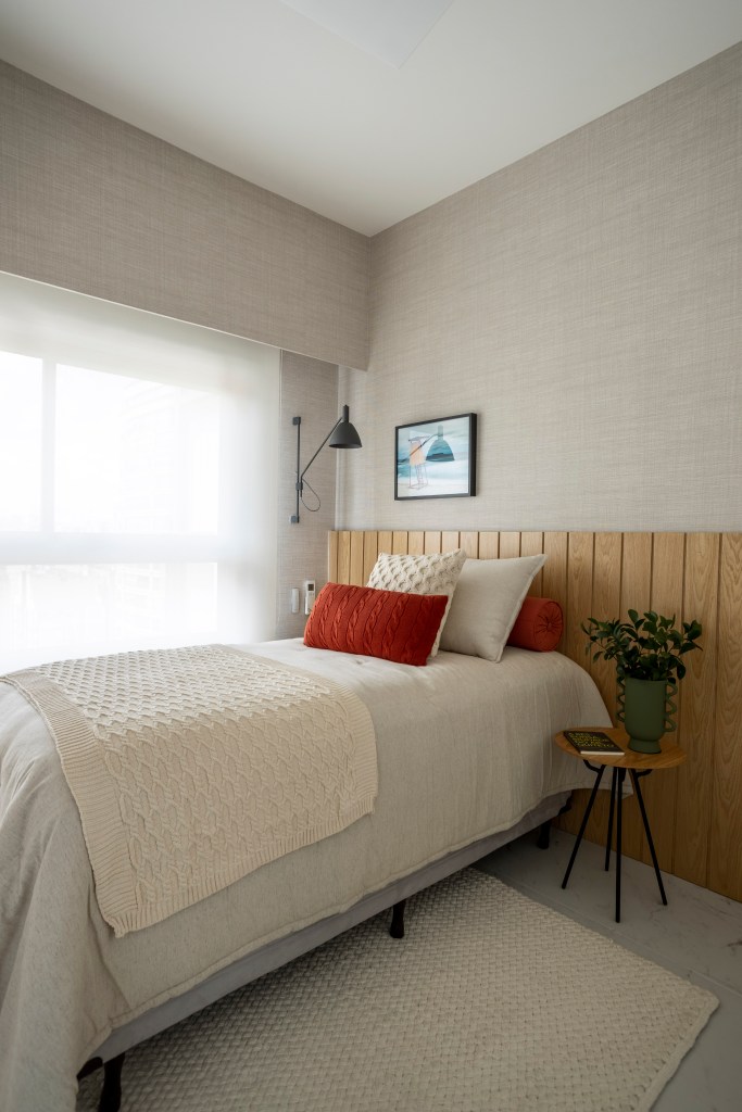 Apê de 110 m² com pé-direito duplo vira duplex com mezanino metálico. Na foto, quarto de hóspedes com cabeceira de madeira e tapete.