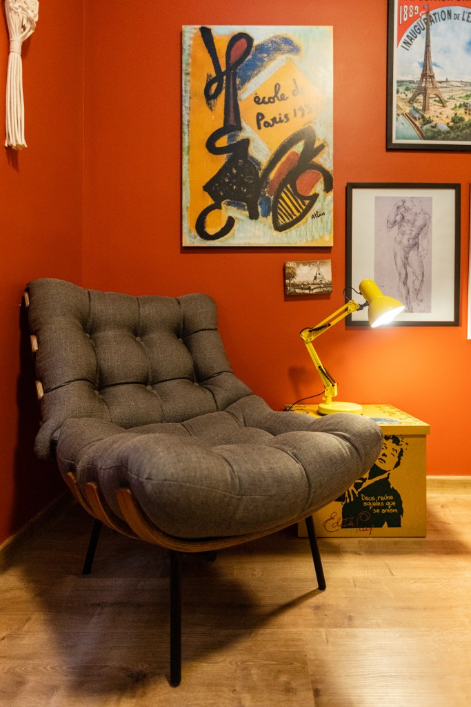 Dicas fáceis para montar um cantinho da leitura em casa. Home office; cantinho de leitura com parede vermelha e poltrona costela cinza. Projeto de Grupo Arquitetos.