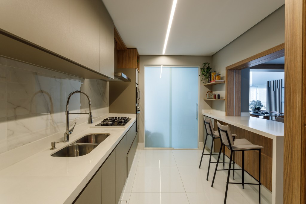 Cozinha com bancada clara, iluminação com fita de LED e marcenaria neutra.