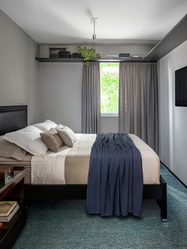 Quarto com cama de casal, cabeceira estofada, mesa lateral e tapete azul.