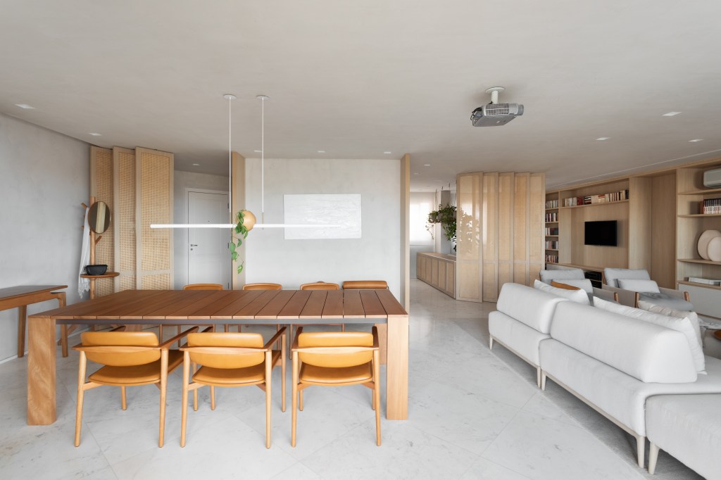 Sala de jantar integrada com estar com piso de mármore, mesa de jantar de madeira, cadeiras de madeira e luminária.