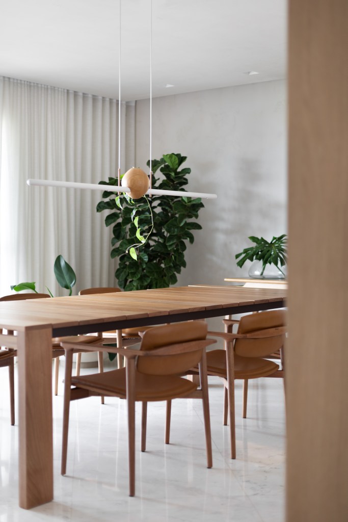 Sala de jantar minimalista com piso de mármore, mesa de madeira, luminária e plantas.