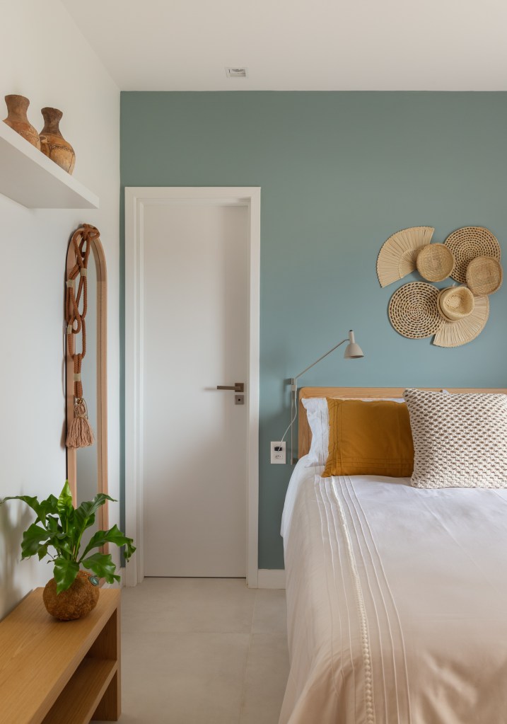 Quarto com parede azul acinzentado, cama de casal e cestarias na parede em cima da cama.