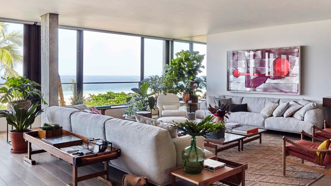 Sala de estar com janela ampla, sofá cinza, tapete, mesa de centro e plantas.