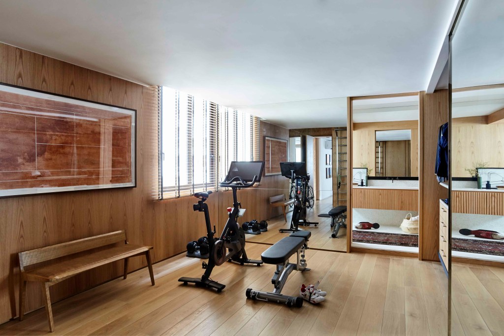 Academia em casa com piso e paredes revestidas de madeira, espelho, bicicleta ergométrica e banco.