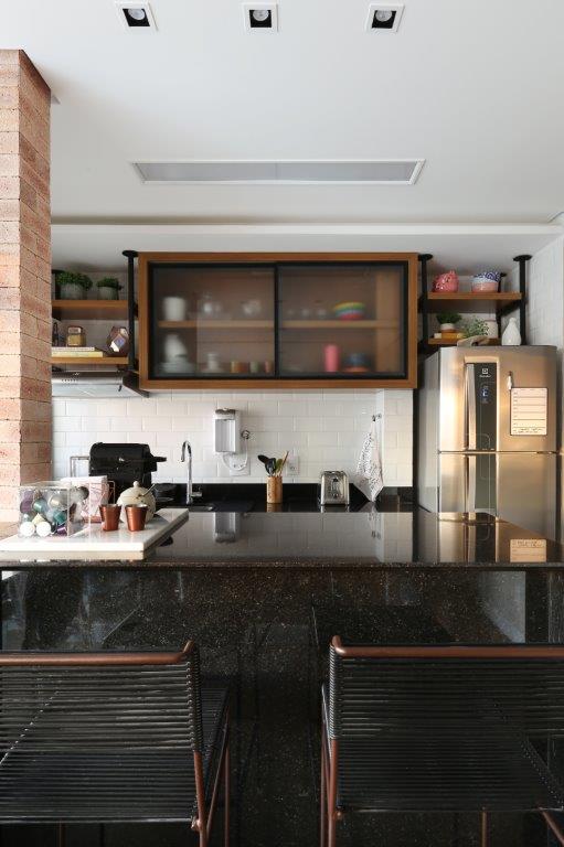 Cozinha integrada com bancada preta e backsplash de tijolinho branco; parede com tijolinhos.