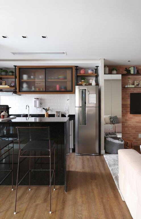 Cozinha integrada com bancada preta e backsplash de tijolinho branco; parede com tijolinhos.