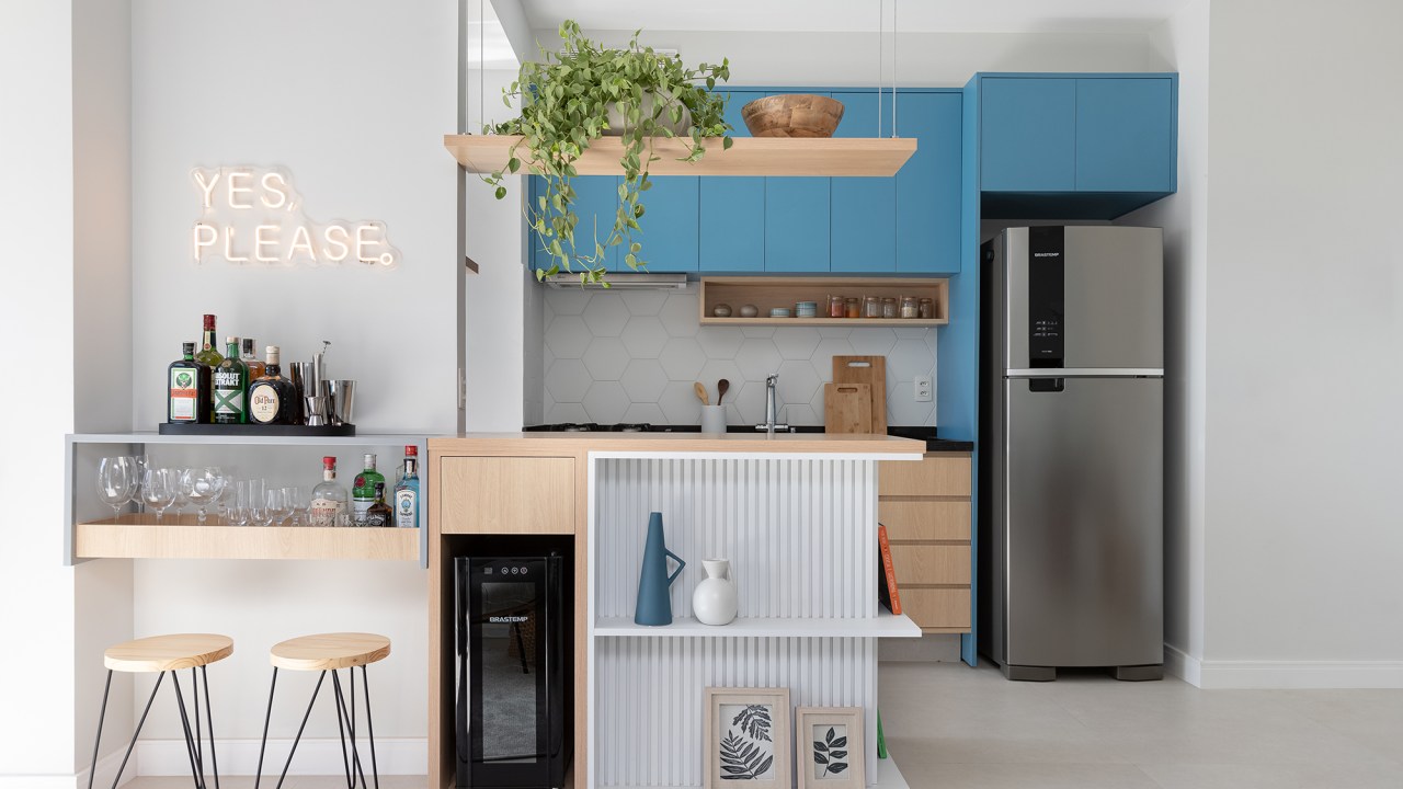 Apê de 56 m² ganha canto alemão com sapateira e bar na bancada da cozinha. Projeto de Thais Monfré, Na foto, cozinha integrada com a sala, bar, bancada ripada e marcenaria azul.